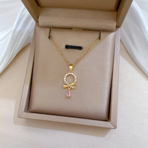Macro detail of gold bow and circle pendant with pink teardrop stone and crystals