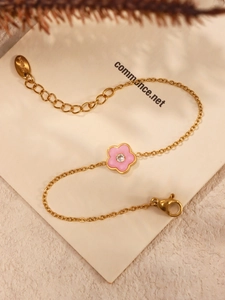 Detail van gouden roestvrijstalen armband met roze emaille bloem en ingelegde zirkoon