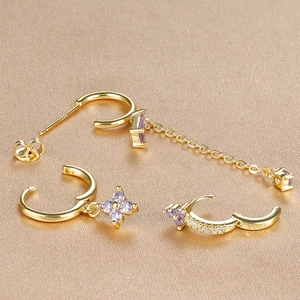 Detail of gold earrings set with purple zircon flower pendants on gold textured fabric
