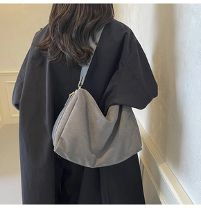 Model showing gray suede pillow bag with wide shoulder strap against a neutral background