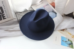 Detail of a dark blue wide-brimmed felt fedora hat shown in a stylish lifestyle setting