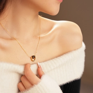 Detailed close-up of a gold U-shaped tiger eye pendant necklace worn by a model in a white sweater