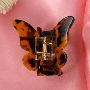 Detailed view of a tortoiseshell butterfly hair claw clip on pink satin fabric background