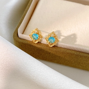 Detailed close-up of vintage gold hollowed-out earring with sea-blue zircon on silk fabric