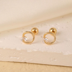 Macro detail of a gold round hoop earring with a sparkling zircon on white silk fabric