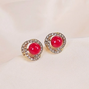 Macro view of gold stud earrings with red beads and clear crystal pavé setting