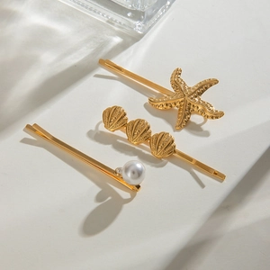 Close-up of 18k gold hair clips featuring starfish, shells, and pearls with light shadows
