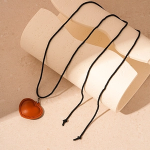 Close-up of brown leather heart pendant with fine stitching on a black cord necklace