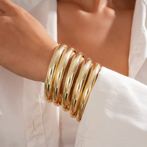 Detail shot of six chunky high-gloss gold minimalist geometric bracelets worn by a model