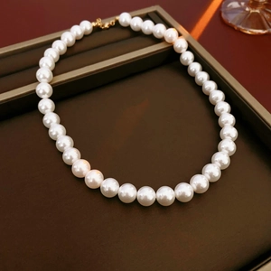 Gros plan d'un collier de perles blanches avec fermoir doré dans un écrin à bijoux brun