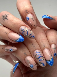 Detail of almond-shaped press-on nails featuring blue evil eye and gold snake motifs