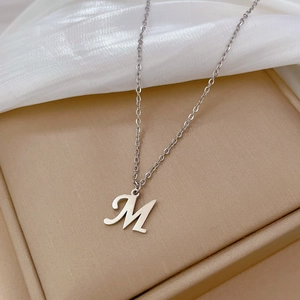Macro detail of silver M letter pendant with fine O-chain on elegant silk background