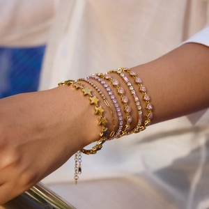 Close-up of stacked gold-tone bracelets with pink heart zircon stones on a wrist