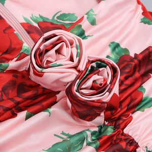 Detail of pink satin floral dress featuring red rose print and 3D fabric rose accents