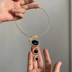 Detail of gold metal choker featuring a spiral pendant with three black oval resin stones