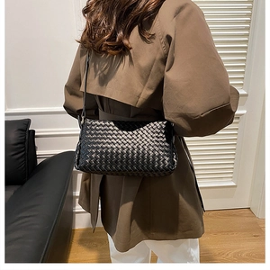 Modella che posa con una borsa a tracolla in pelle intrecciata nera e un trench marrone