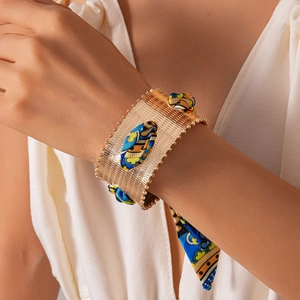Detail of vintage gold textured metal cuff bracelet with bohemian ethnic printed silk ribbon