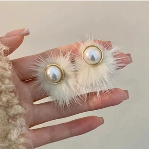 Close-up of fluffy white fur ball earrings with pearl center and golden metal frame