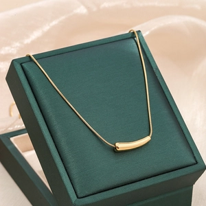 Close-up of a minimalist gold eggplant pendant necklace on a green jewelry box