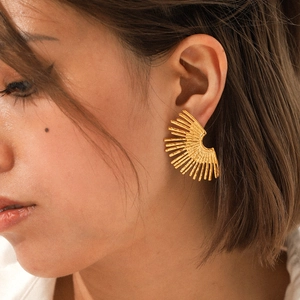 Close-up of a gold-toned fan-shaped earring with radiating lines worn by a female model