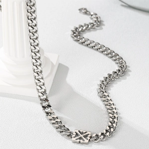 Detail of silver titanium Cuban link necklace with cross pendant on white pedestal