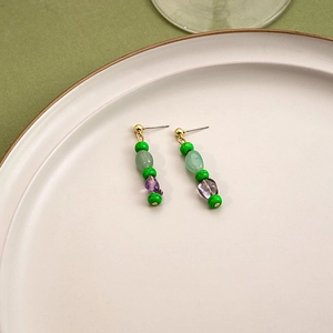 Detail of beaded earrings with green and purple resin stones on white ceramic plate