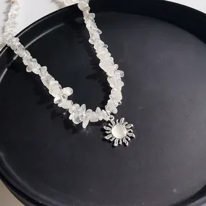 Bohemian white crystal gravel necklace with silver sun pendant on a black plate