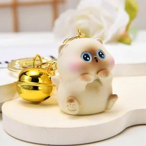 Close-up of cute beige Siamese cat keychain with gold bell and metallic ring details