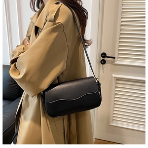 Close-up of minimalist black leather crossbody bag styled with a beige trench coat