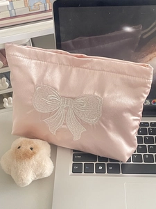 Detailed embroidery of white bow on pink satin makeup bag with smooth texture and zipper