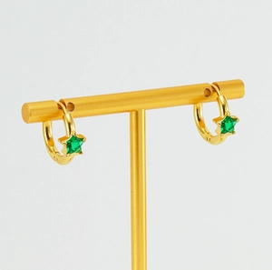 Détail de créoles dorées avec zircon étoile vert étincelant sur porte-bijoux