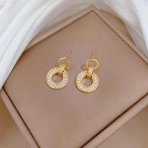 Close-up of golden interlocking rings earrings with white pavé zircons on silk