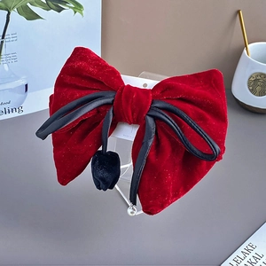 Detail of red velvet bow hair clip with black fur pompom and pearl tassel pendant