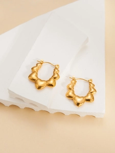Detail of gold heart-shaped hoop earrings displayed on white geometric props