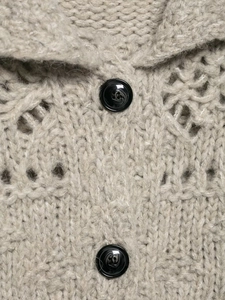 Detailed close-up of hollow knit texture and black buttons on beige knitted cardigan