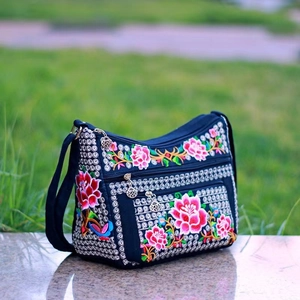 Close-up of floral embroidery on black canvas crossbody bag with silver zipper pulls