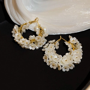 Macro detail of golden flower cluster C-shaped hoop earrings with pearly white petals