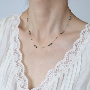 Detail of beaded turquoise and burgundy necklace worn over a white lace garment
