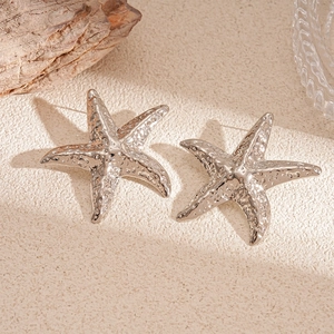 Close-up of starfish earrings with textured silver finish on a natural textured surface