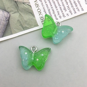 Macro view of two glitter resin butterfly pendants with green and blue gradient finish