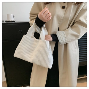 Detail shot of white corduroy tote bag showing soft ribbed texture on beige coat