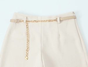 Dettaglio cintura a catena dorata con fibbia in pelle su pantaloncini beige a vita alta