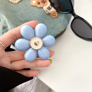 Close-up of blue flower phone socket grip with golden heart center on denim backdrop