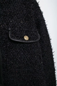 Détail de veste en tweed noir avec poche bordée de cuir et bouton doré en relief