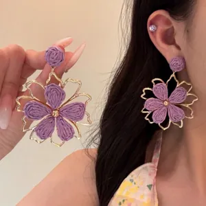 Dettaglio di grandi orecchini a fiore intrecciato viola con eleganti cornici dorate
