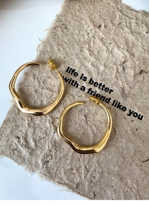 Top view of gold irregular geometric hoop earrings on textured paper with artistic lighting