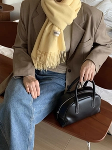 Close-up of yellow tassel scarf with white label and black leather handbag detail