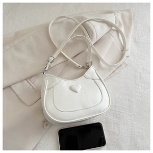 Flat lay of white half-moon crossbody bag with heart detail and shoulder strap