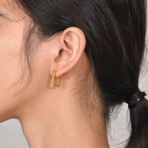 Close-up of a minimalist golden rectangular geometric hoop earring worn by a model