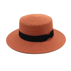 Detailed close-up of orange-red boater hat featuring a stylish black grosgrain ribbon bow